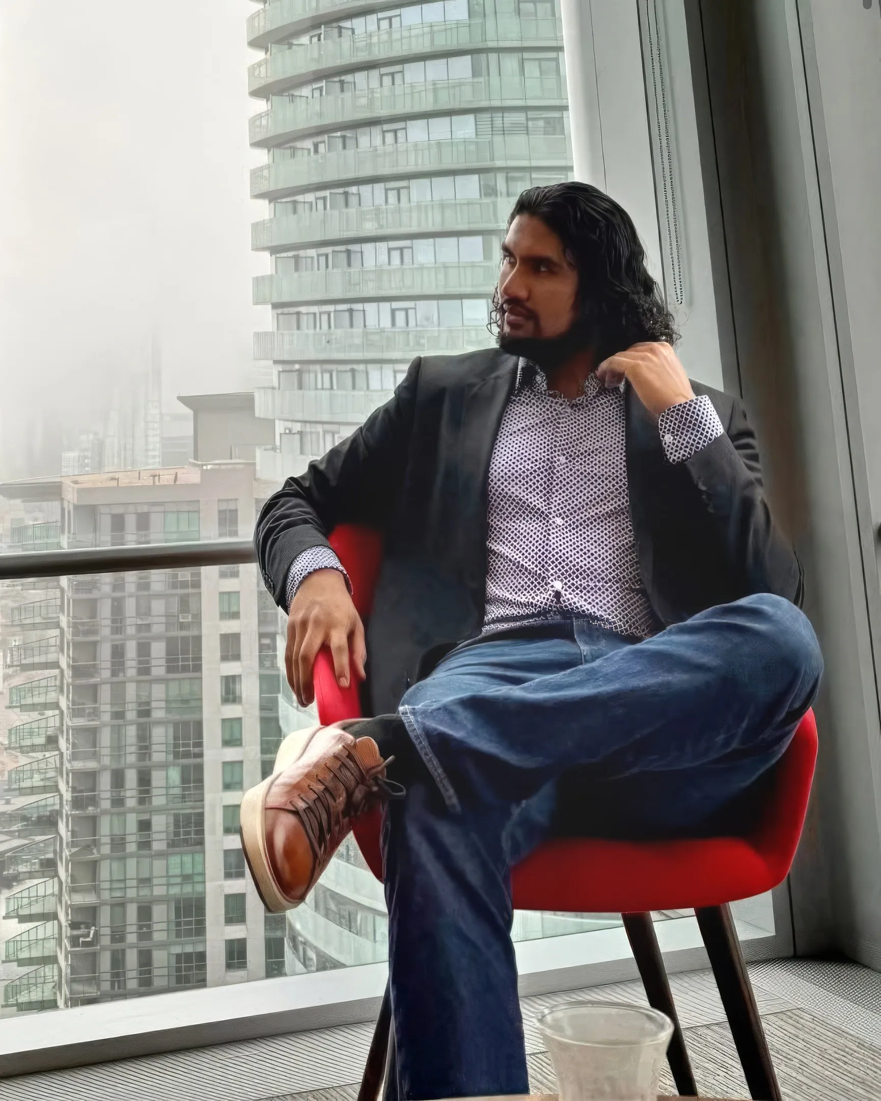 Kubera Desai seated in a red chair by a high-rise window, the city behind him