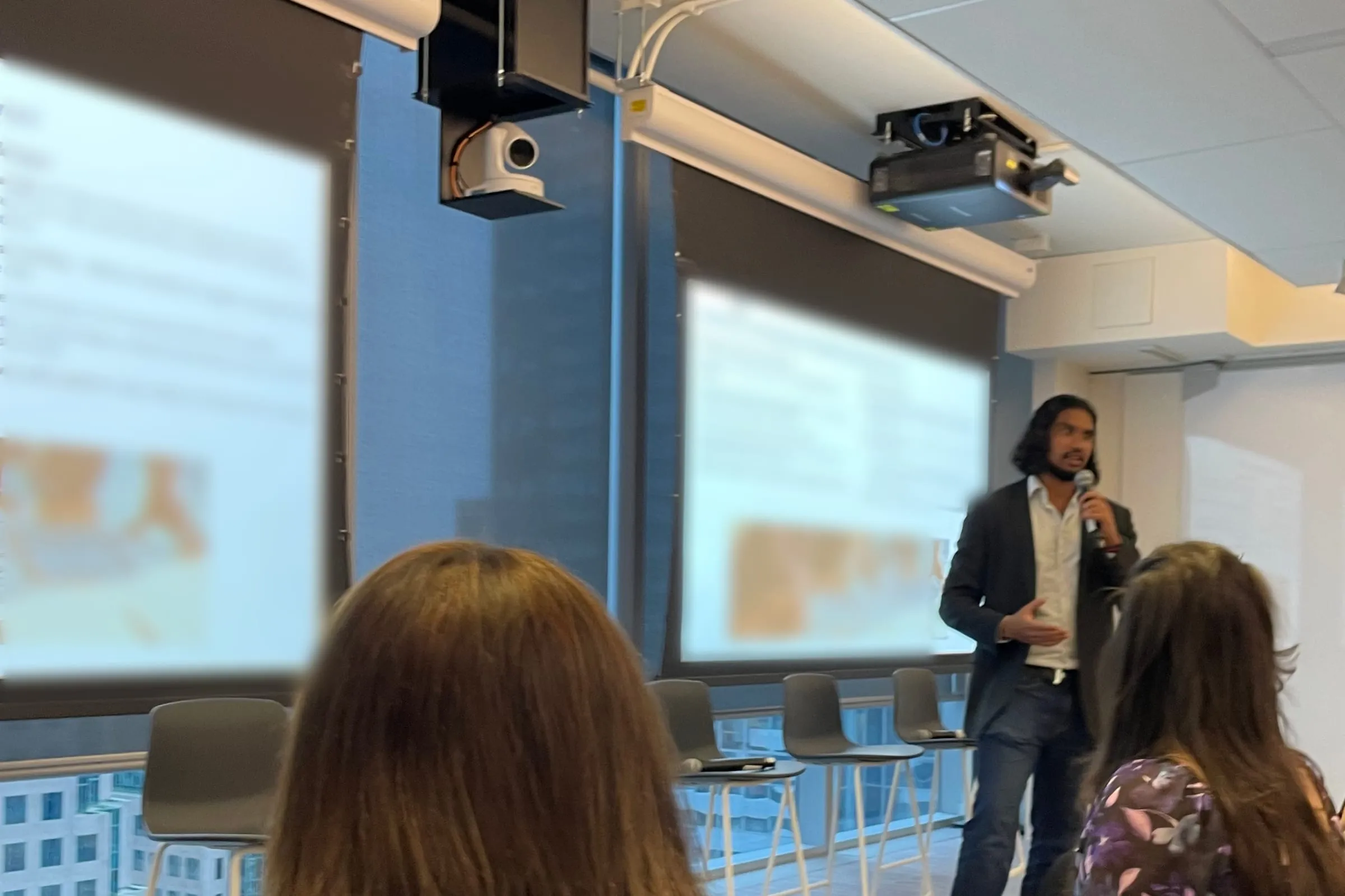 Kubera presenting to a room, with slides on two screens behind him